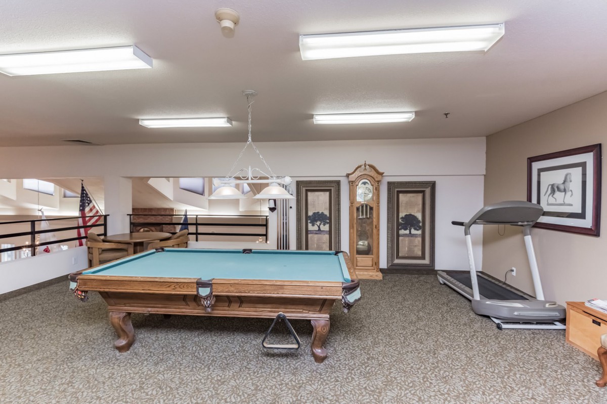 A recreational room featuring a pool table, treadmill, and a grandfather clock under bright indoor lighting.