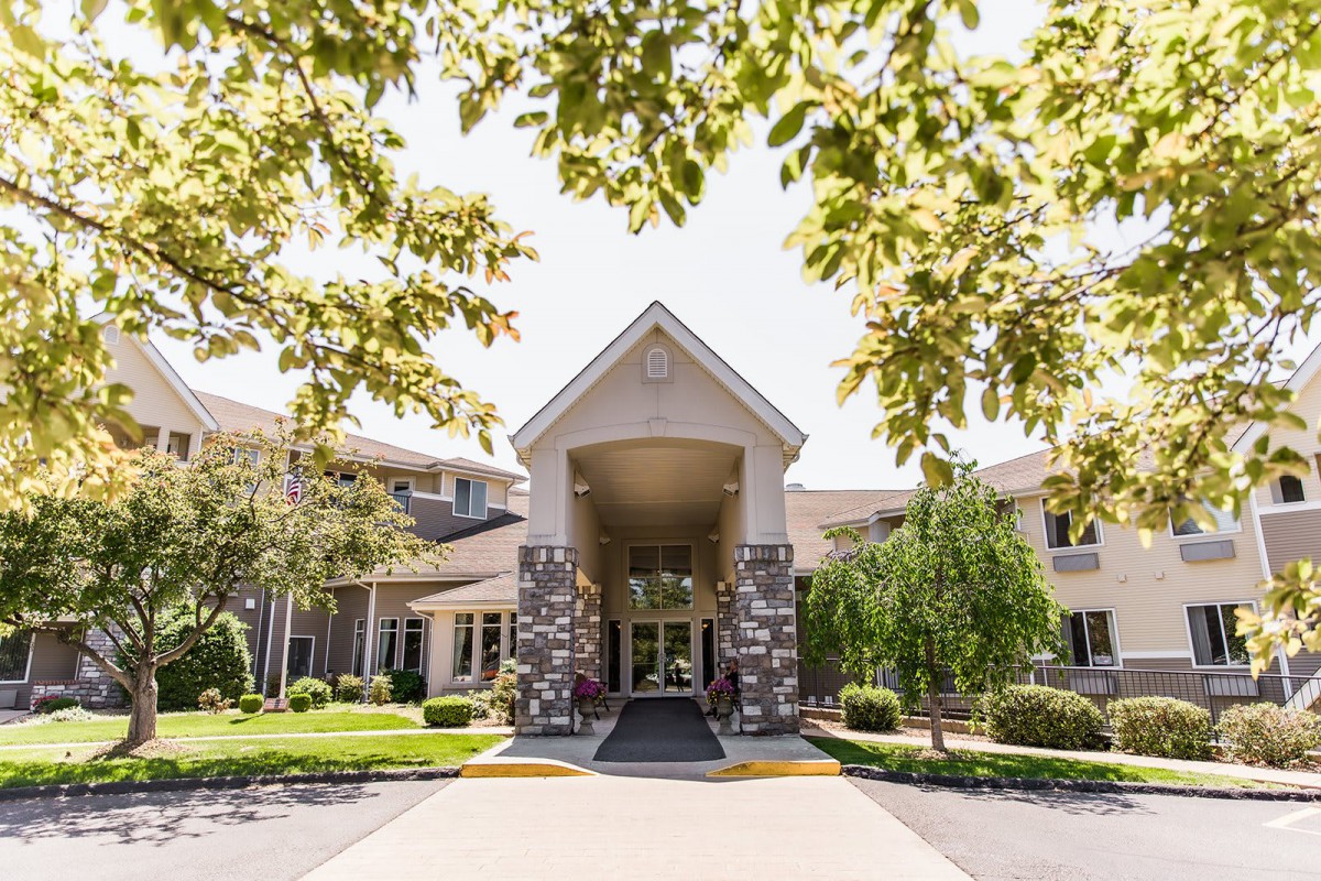 A view of a building entrance surrounded by trees and landscaping on a sunny day.