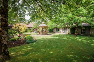A tranquil garden with a gazebo surrounded by lush greenery and a well-maintained lawn.