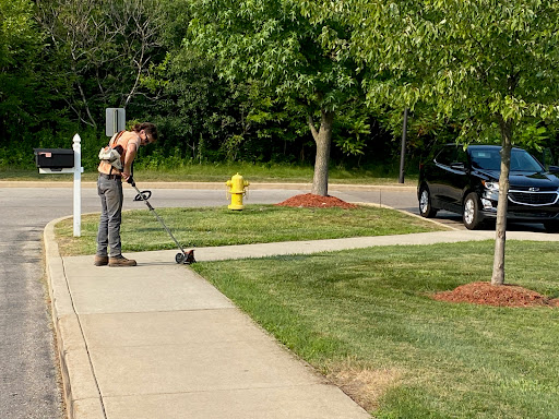 A man uses a string trimmer to tidy up the edges of a sidewalk in a well-maintained yard.
