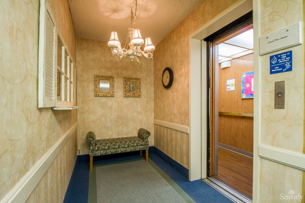 A neatly decorated hallway with an open elevator, a bench, and a chandelier.
