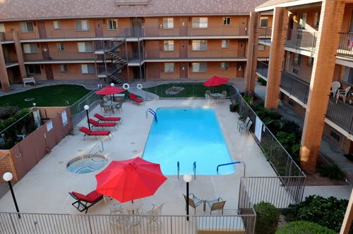 An outdoor hotel swimming pool surrounded by red umbrellas and lounge chairs.