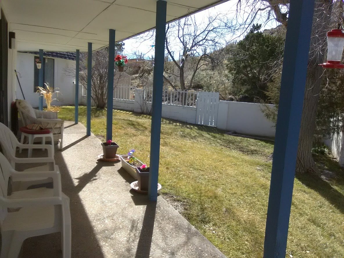 A sunny backyard with a covered patio and a fenced lawn area.