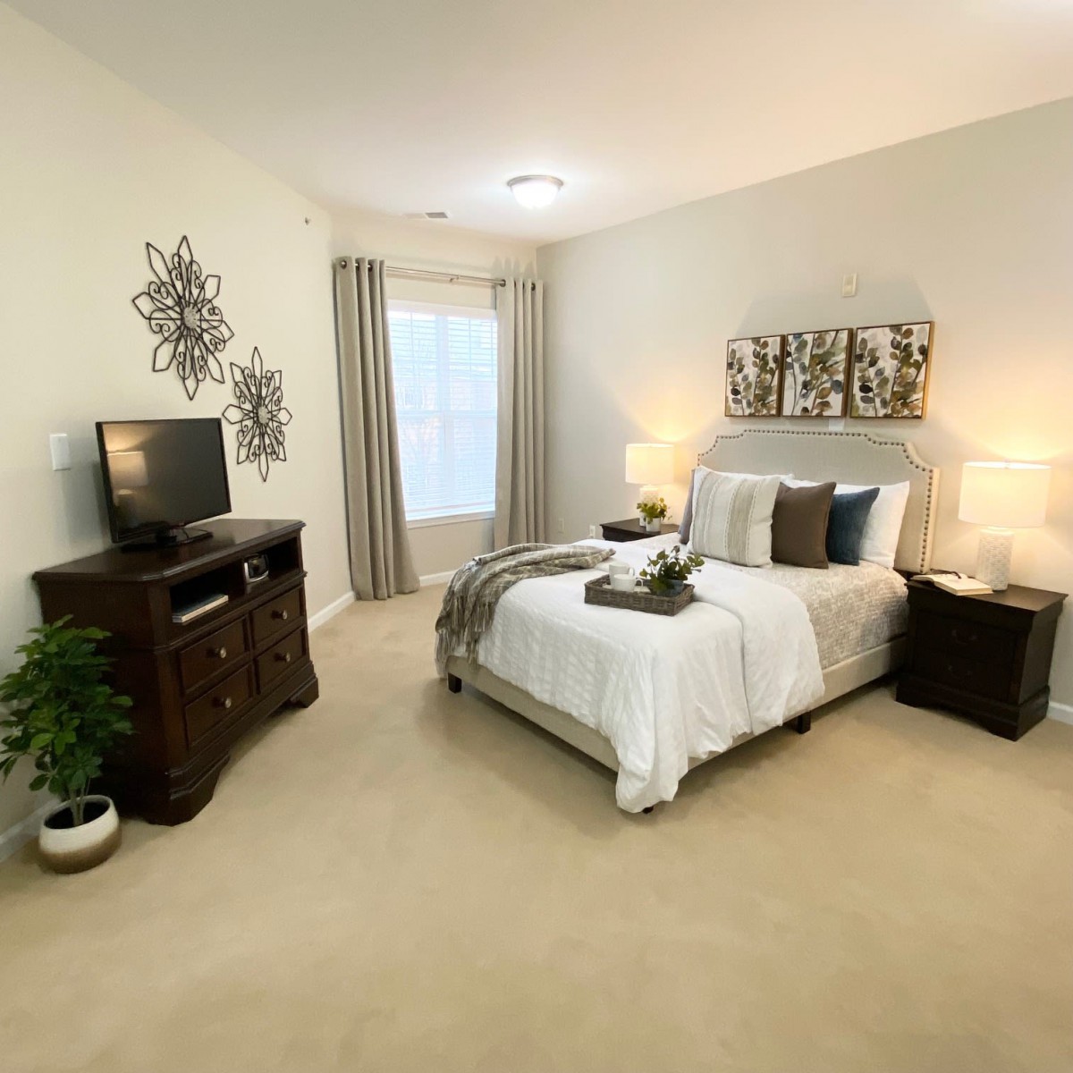 A cozy and well-decorated bedroom with a bed, nightstands, lamps, a TV stand, and a small potted plant.