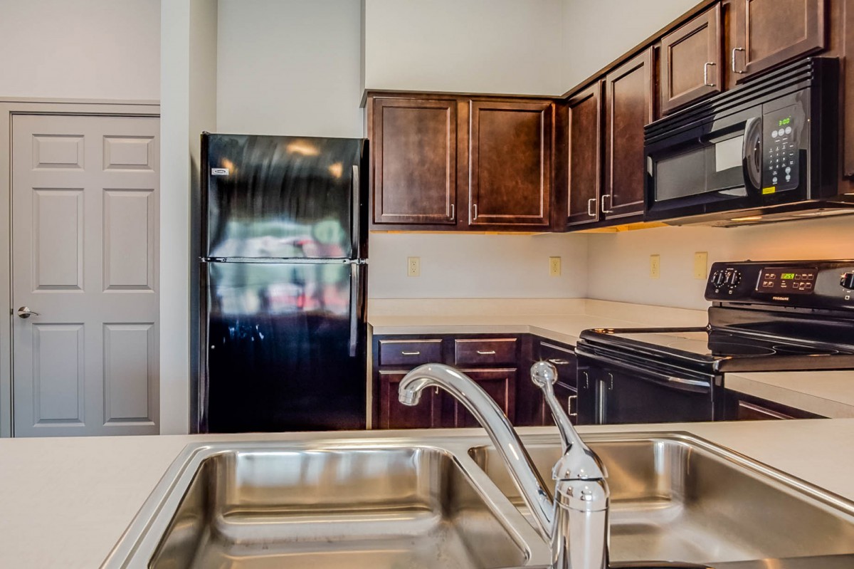 A modern kitchen with a stainless steel sink, wooden cabinets, and black appliances.