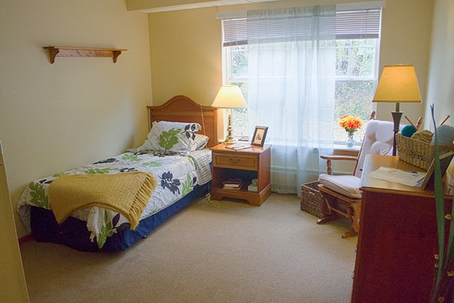 A cozy bedroom with a single bed, nightstand, and window with sheer curtains.