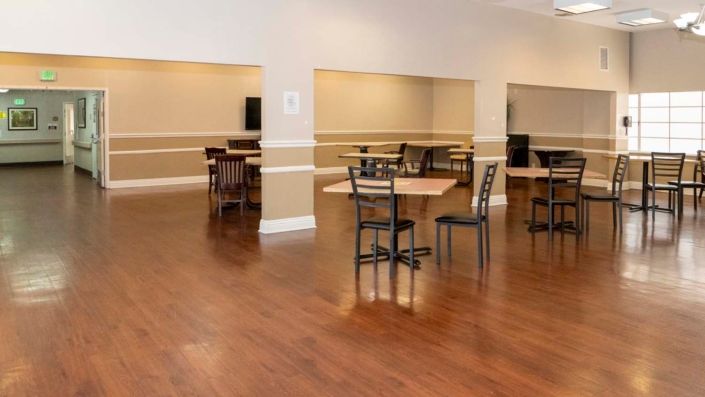 A spacious, empty room with wooden flooring, furnished with tables and chairs arranged for dining or meetings.