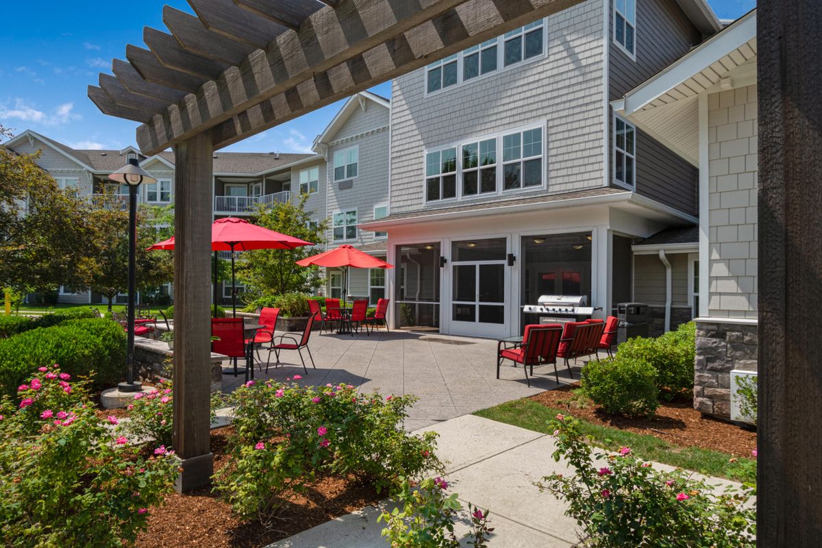 A sunny outdoor patio area with red umbrellas and a residential building backdrop.