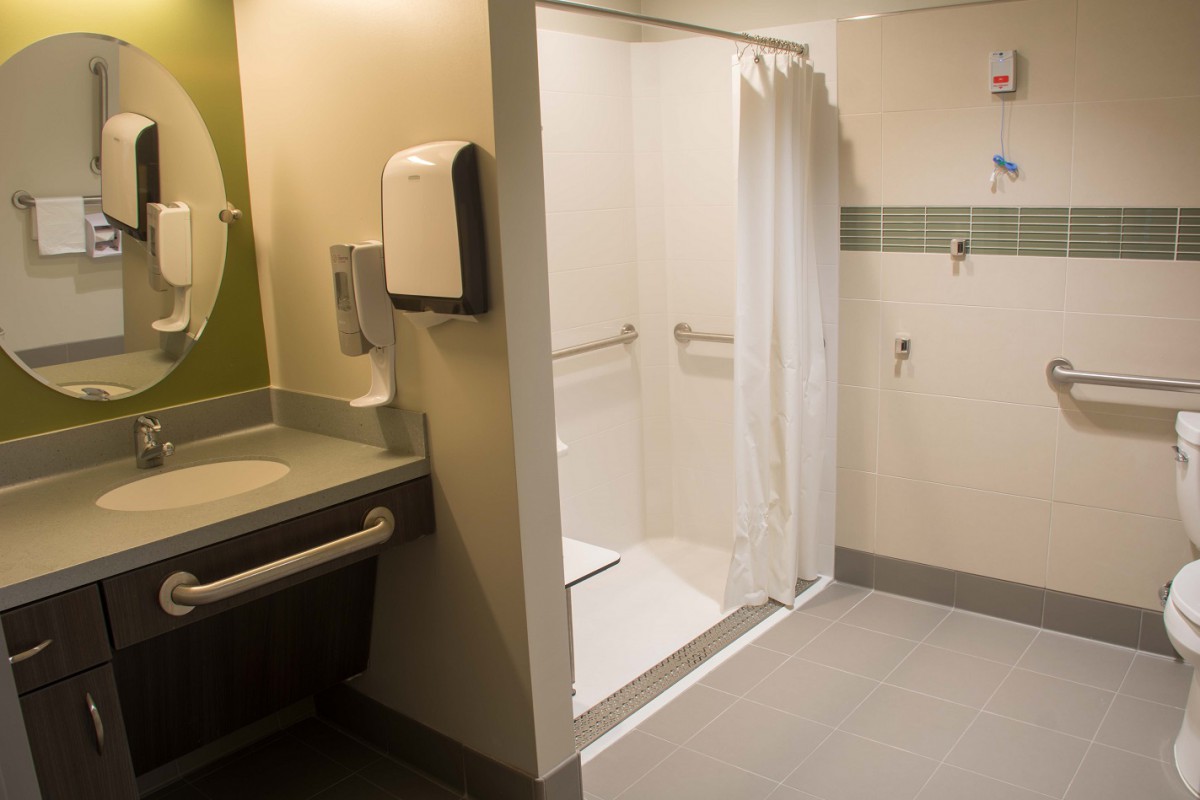 A modern, accessible bathroom featuring a shower with grab bars and a curtain alongside a sink.