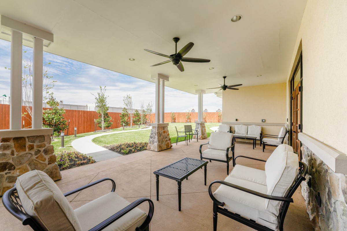 Spacious patio with comfortable seating and ceiling fans overlooking a landscaped yard.