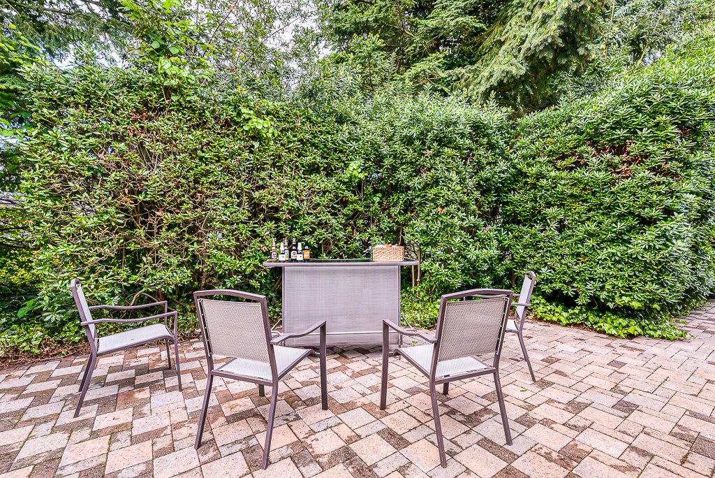 A cozy outdoor patio area with chairs and a small table surrounded by lush greenery.