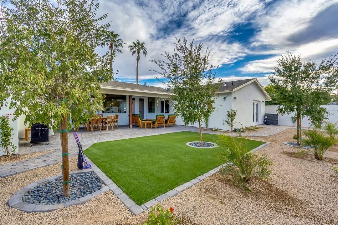 A cozy house with a landscaped yard, featuring a small patio and lush greenery under a partly cloudy sky.