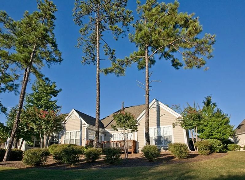 A suburban house surrounded by tall trees on a sunny day.