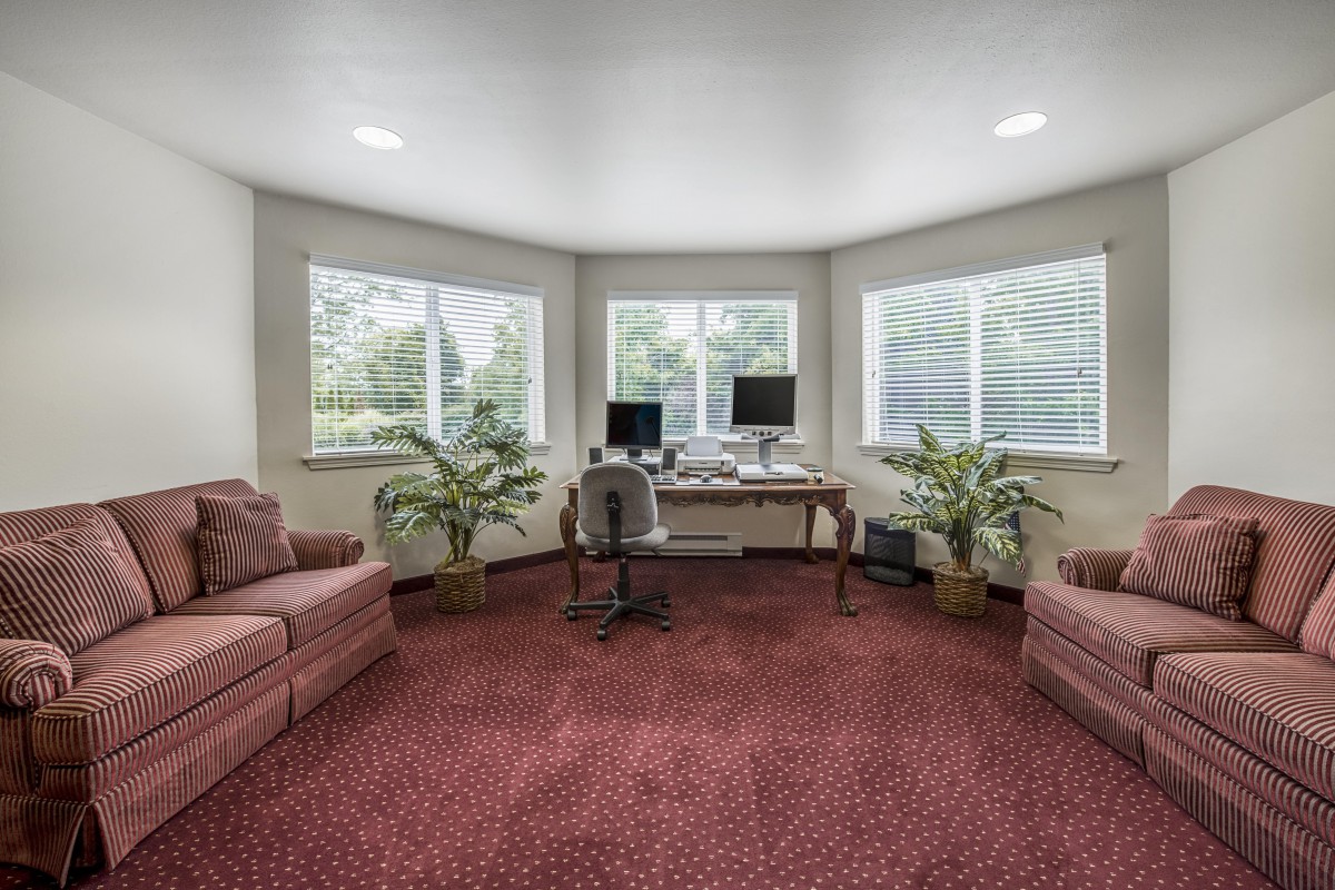 A cozy home office with a computer desk, two sofas, and large windows allowing natural light.