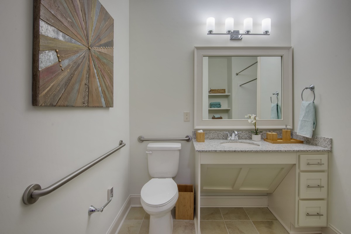 A modern bathroom with a toilet, vanity, and mirror, featuring sleek design elements.