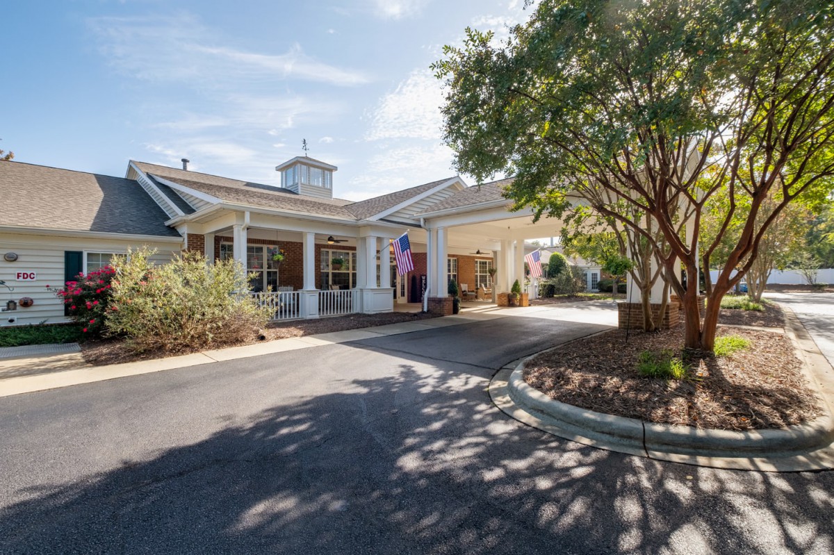 An entrance view of a building with a driveway surrounded by trees and landscaping under a clear sky.