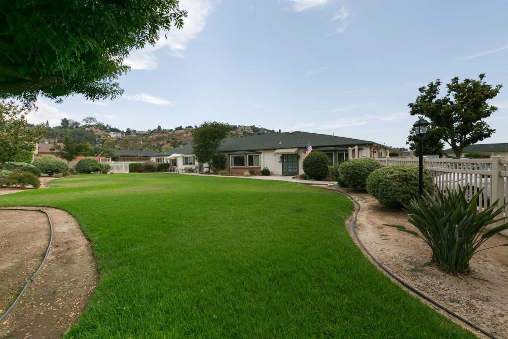 A scenic view of a house with a large green lawn and surrounding trees.