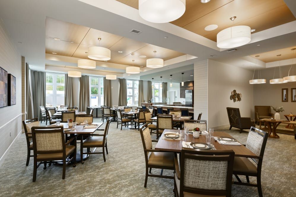 A spacious dining area featuring well-arranged tables and chairs, complemented by modern lighting and large windows.