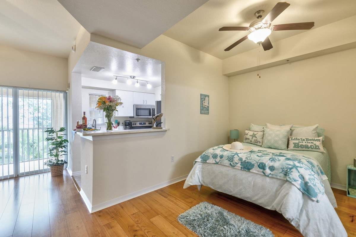 A cozy studio apartment with an open kitchen and a neatly arranged bed.