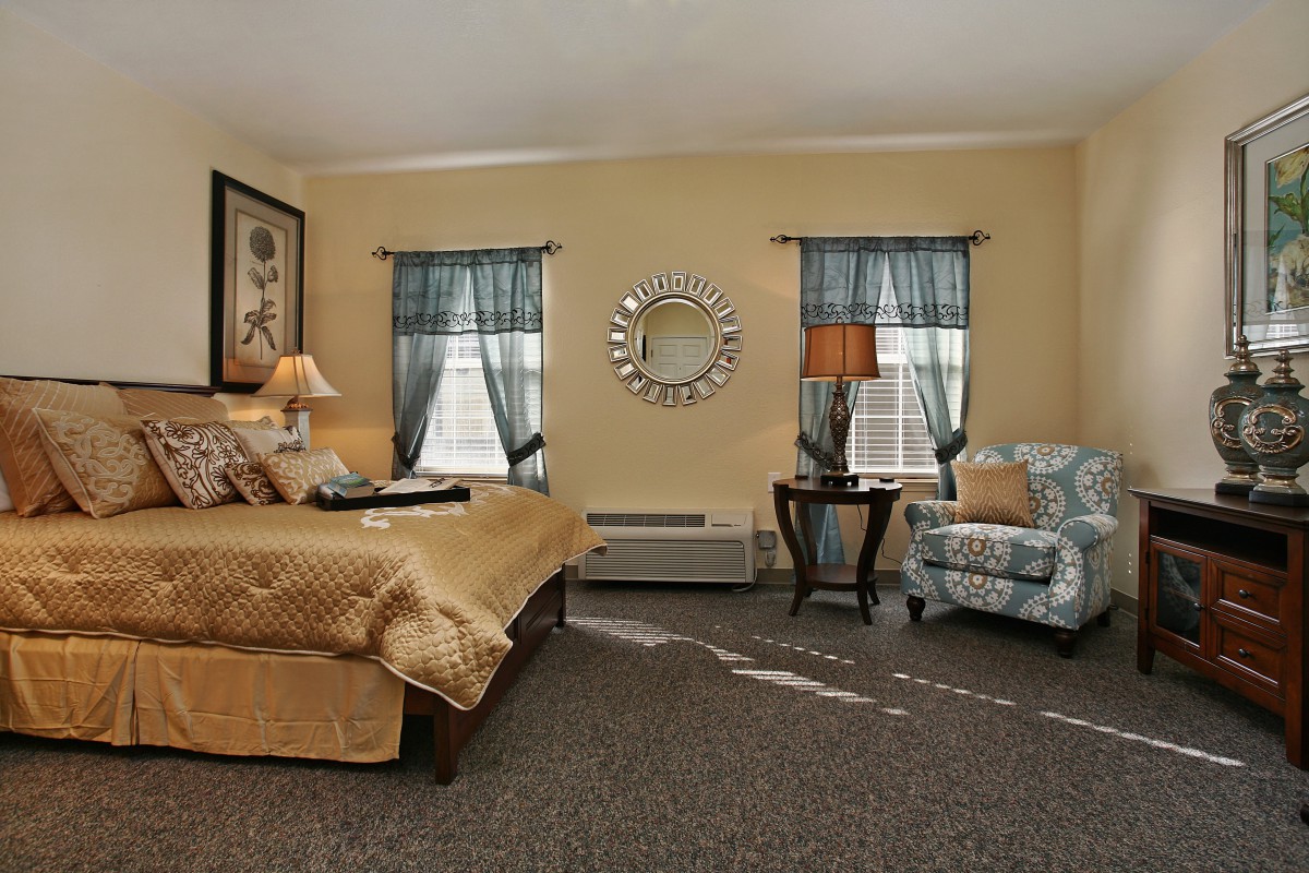 A cozy bedroom with a large bed, armchair, and elegant decor including a mirror and lamps.