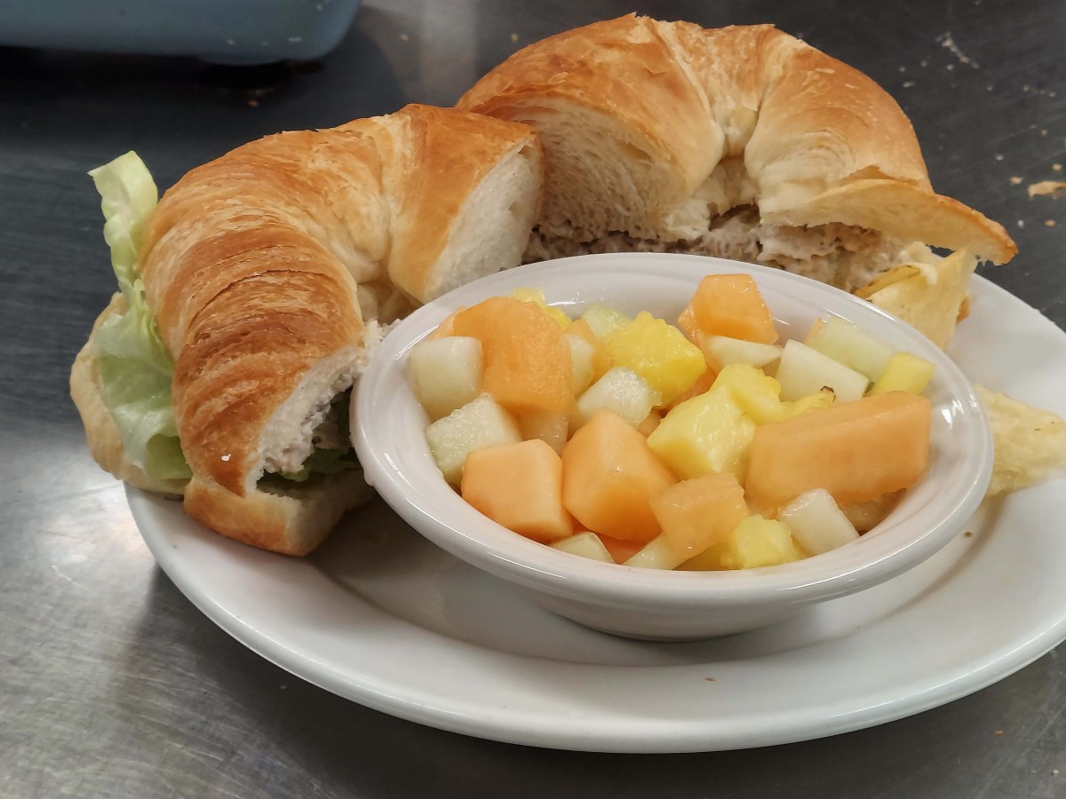 A breakfast plate featuring a croissant and a bowl of mixed fruit salad.