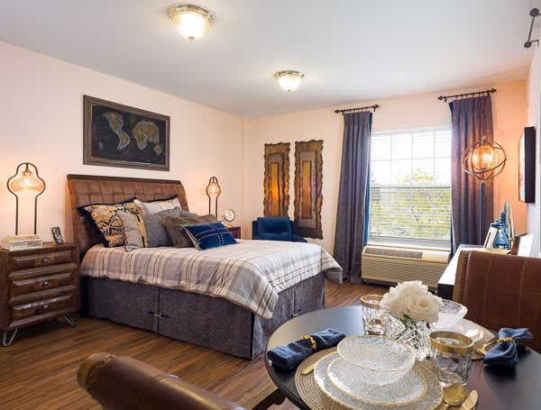 A cozy bedroom with a double bed, decorative pillows, and elegant curtains next to a dining area.