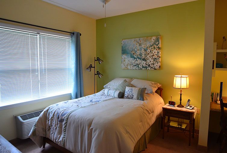 A cozy bedroom featuring a neatly made bed, a lamp on the nightstand, and a window with curtains.