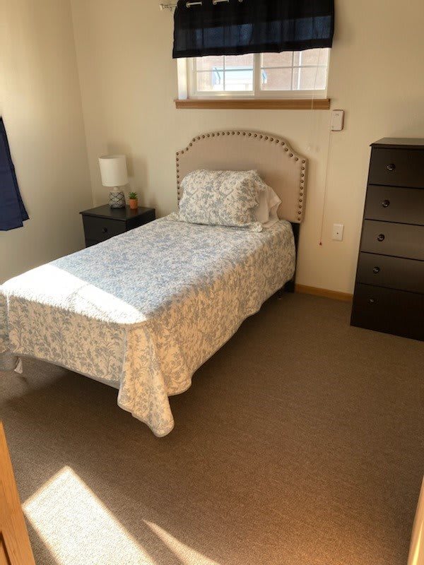 A small bedroom with a single bed, nightstand, lamp, and dresser.