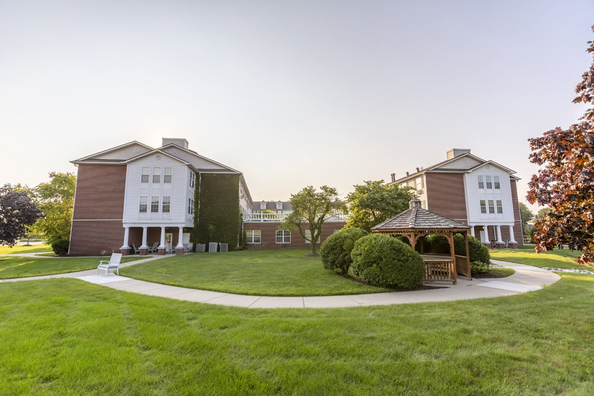 A peaceful courtyard featuring two buildings, a well-maintained lawn, and a charming gazebo surrounded by greenery.