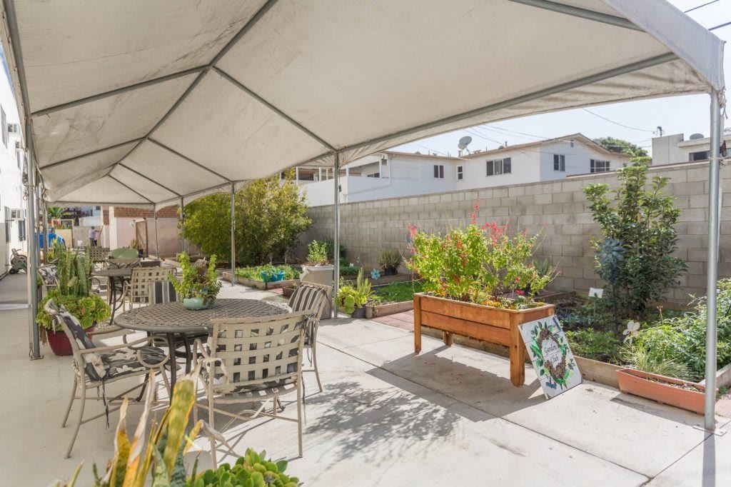 A covered outdoor patio area with tables, chairs, and raised garden beds.