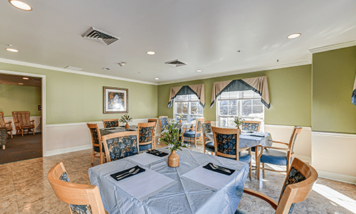 A cozy dining area with tables set for a meal, featuring tablecloths, decorations, and large windows with curtains.