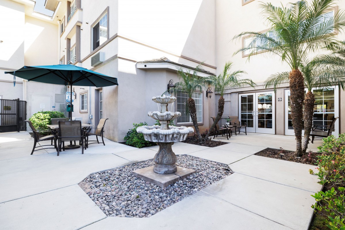 A serene courtyard featuring a multi-tiered fountain surrounded by outdoor seating and palm trees.