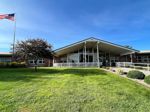 A modern building set against a clear blue sky, surrounded by lush green grass and trees.