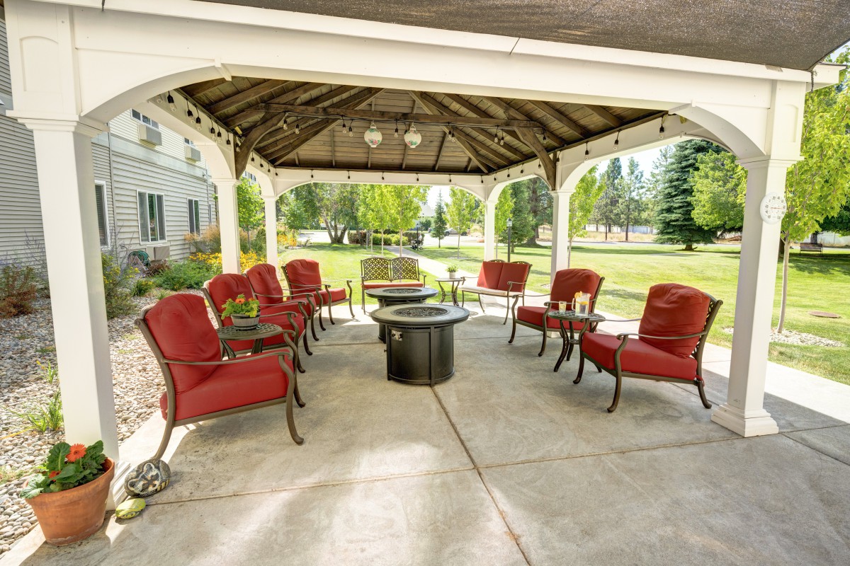 A cozy outdoor gazebo featuring red cushioned patio furniture and a central fire pit, surrounded by a scenic landscape.