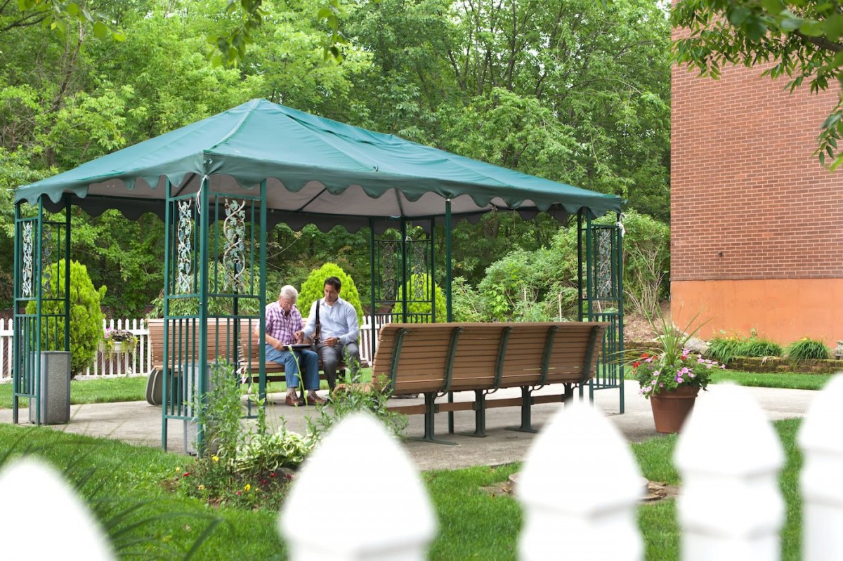 An elderly couple sitting and relaxing in a gazebo surrounded by lush greenery.