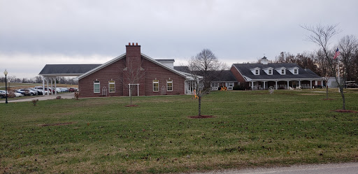 A view of a brick building surrounded by grass and a young tree on a cloudy day.