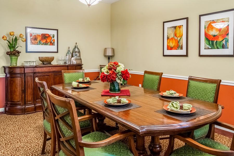A well-decorated dining room with a wooden table, green cushioned chairs, and colorful artwork on the walls.