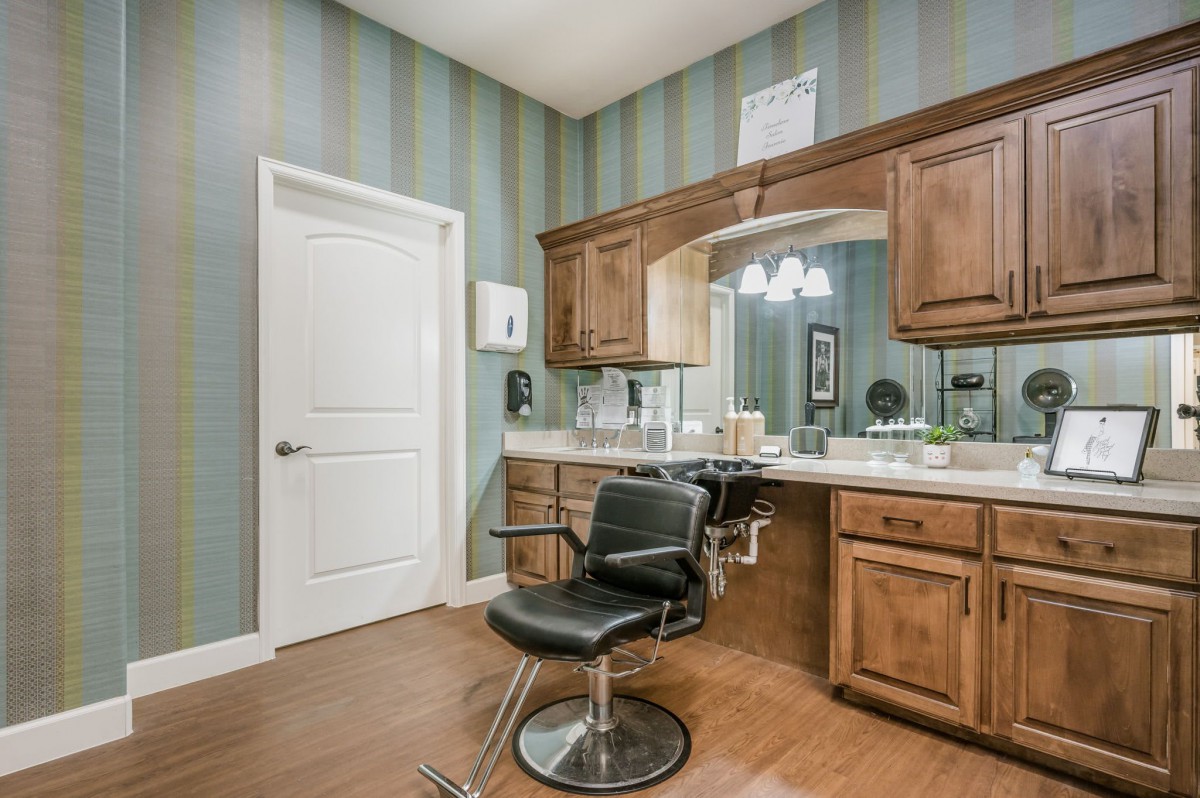 A modern hair salon interior with a styling chair, large mirror, and wooden cabinetry against a striped wall.