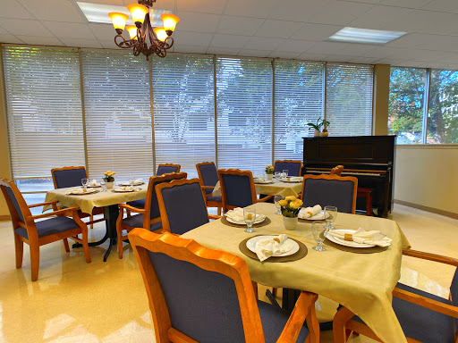 A cozy dining area with set tables, natural light streaming in through the windows, and a piano adding to the ambiance.