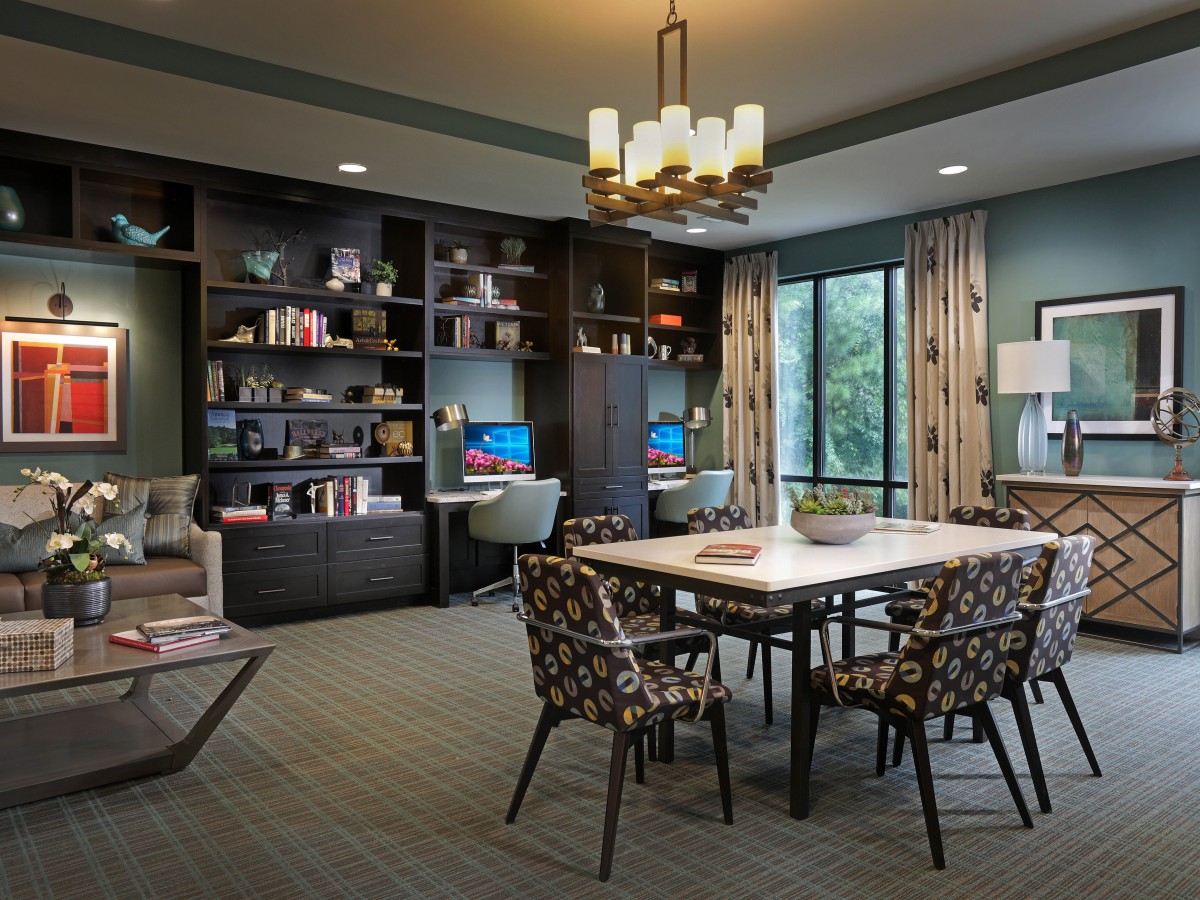 A modern dining room with a table and chairs, surrounded by bookshelves and illuminated by a chandelier.