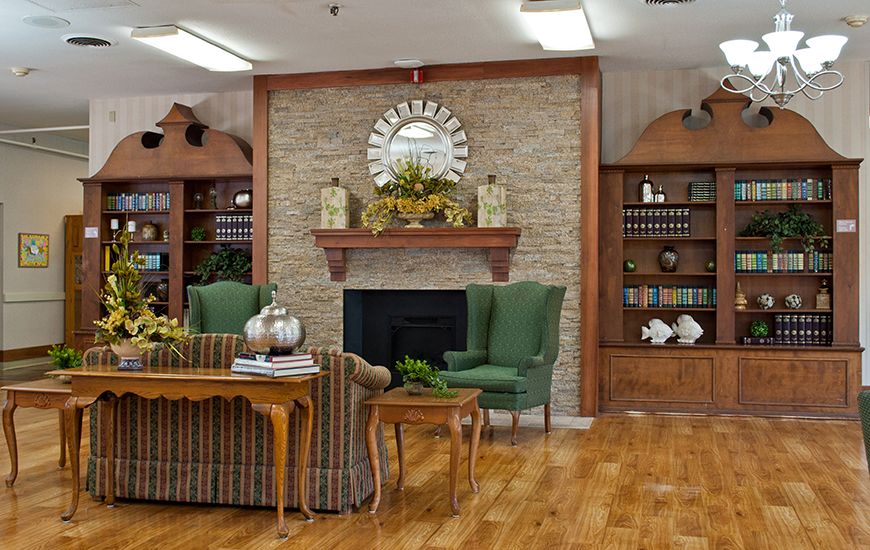 A cozy living room with a stone fireplace, green armchairs, and bookshelves.