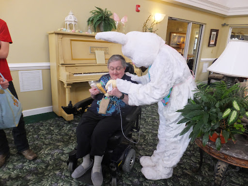 A cheerful Easter celebration at an assisted living facility, where a person in a bunny costume engages with a resident in a wheelchair.