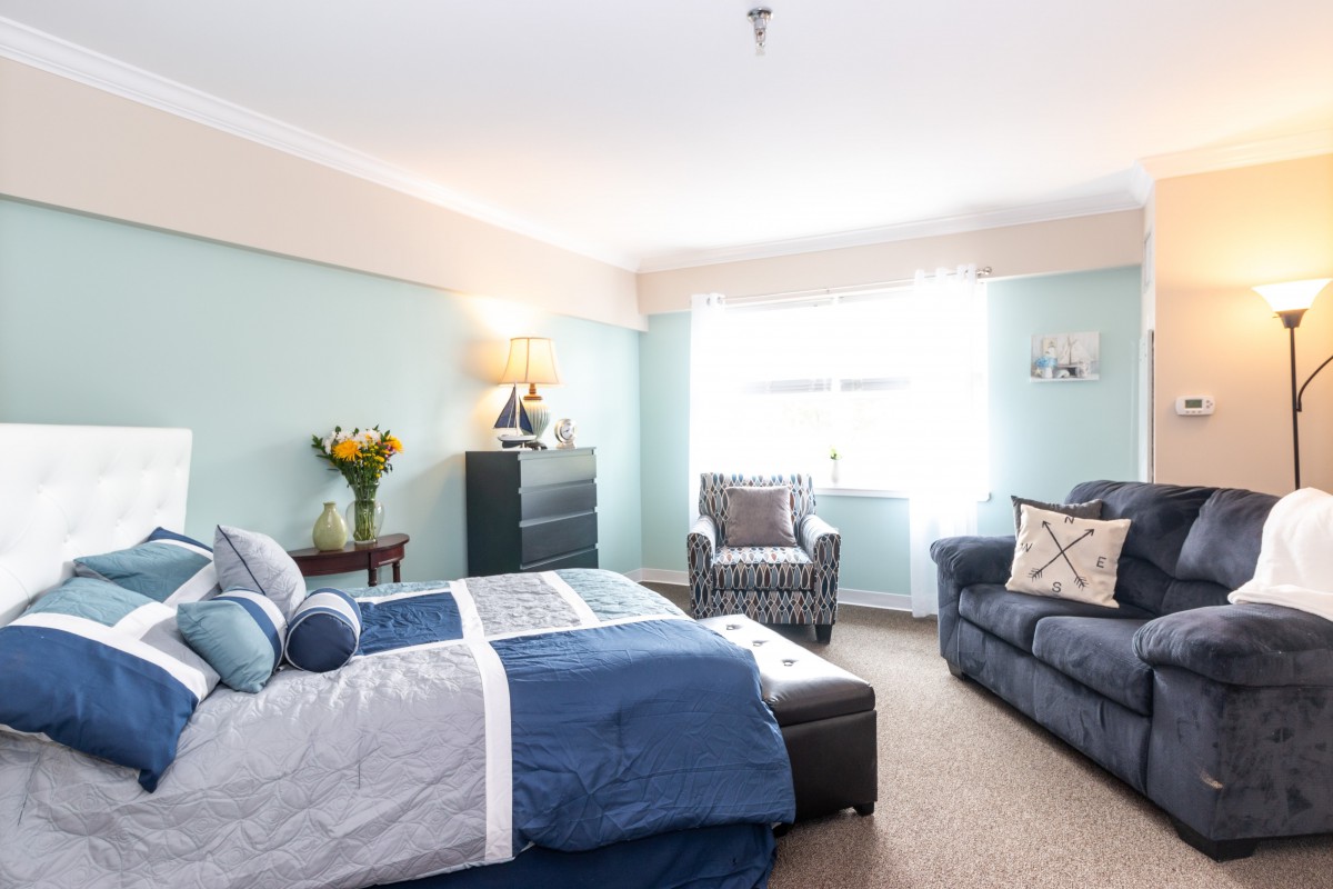 A cozy bedroom with a blue and gray color scheme, featuring a bed, sofa, armchair, and decor.