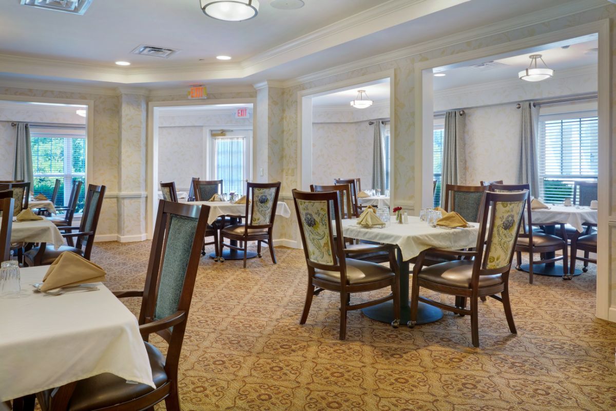An elegant dining room with neatly arranged tables and chairs, featuring a carpeted floor and ample natural light.