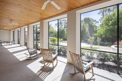 A sunny patio with rocking chairs and large windows overlooking a garden.