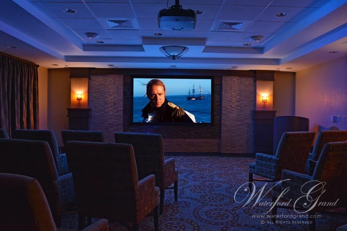 A cozy home theater room with a large screen displaying a movie, surrounded by comfortable seating and dim lighting.