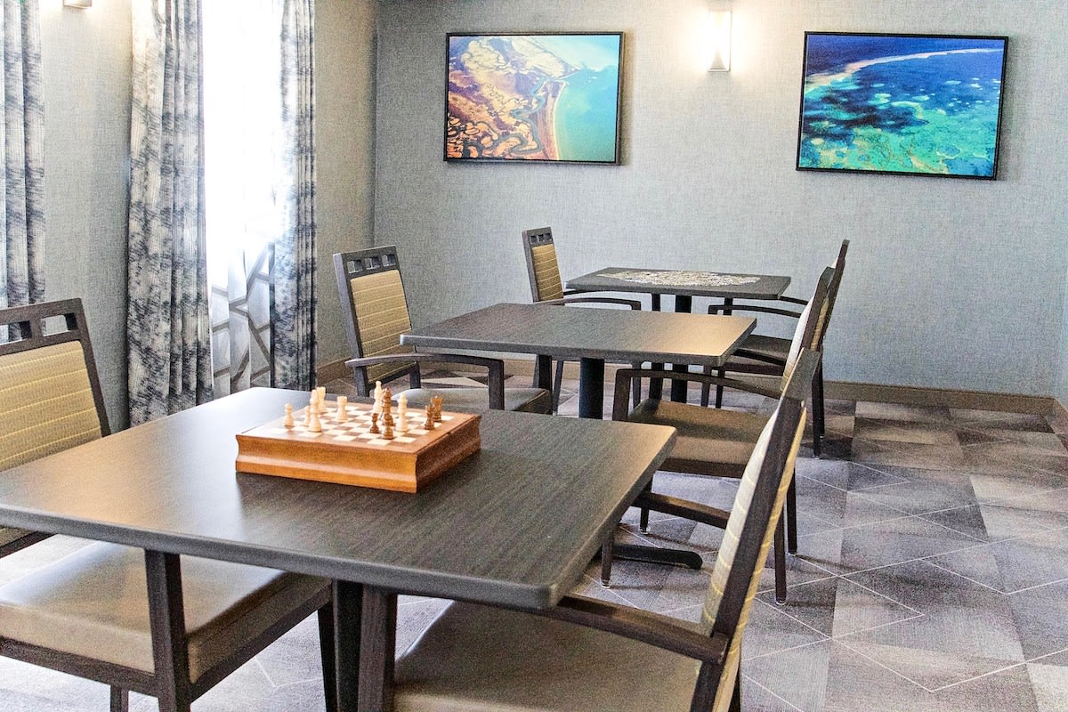 A modern game room with chess set on the table, surrounded by chairs and artistic wall decor.