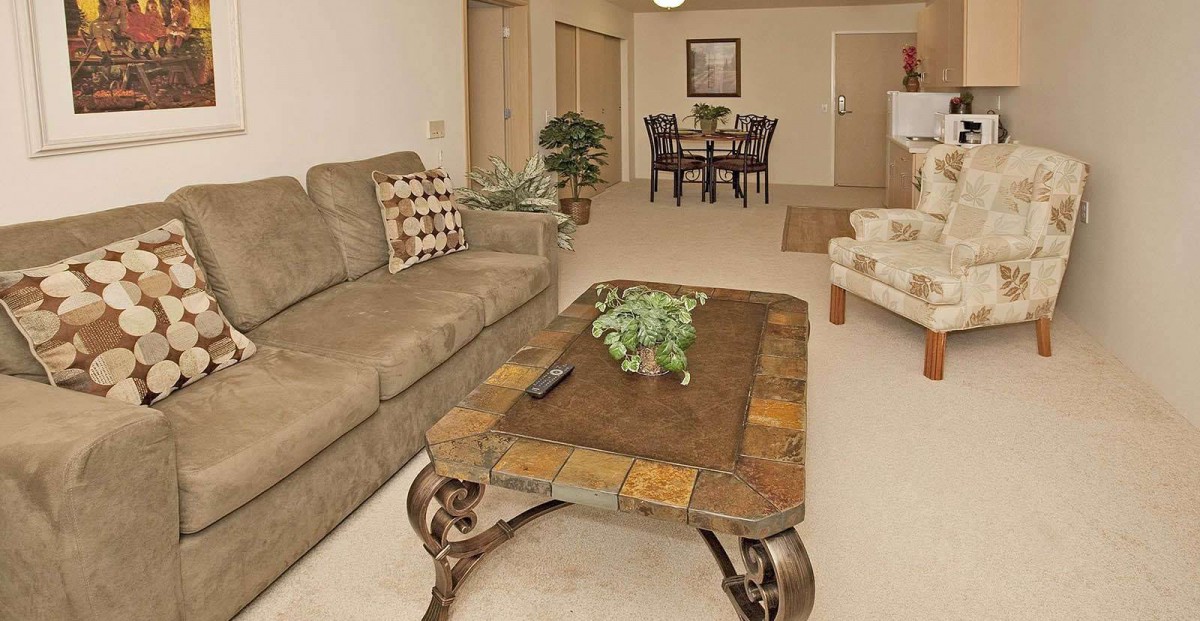 A cozy living room with a sofa and coffee table leading to a dining area in the background.