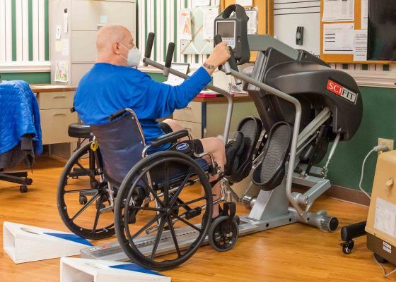 An elderly person in a wheelchair using exercise equipment for rehabilitation.