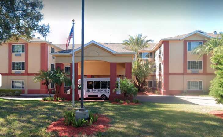 A hotel entrance with a vehicle parked under the canopy, surrounded by palm trees and landscaping.